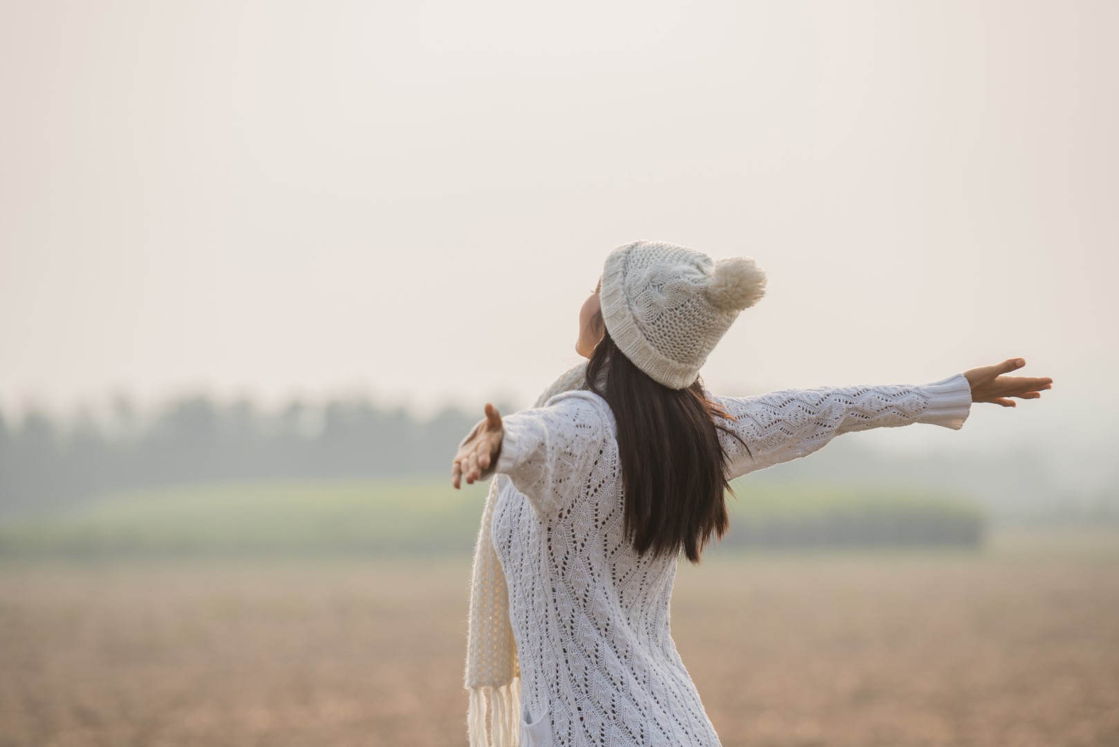 Happy woman enjoying in idyllic nature, celebrating freedom and rising her arms while standing toward the setting sun. Lifestyle and success concept.